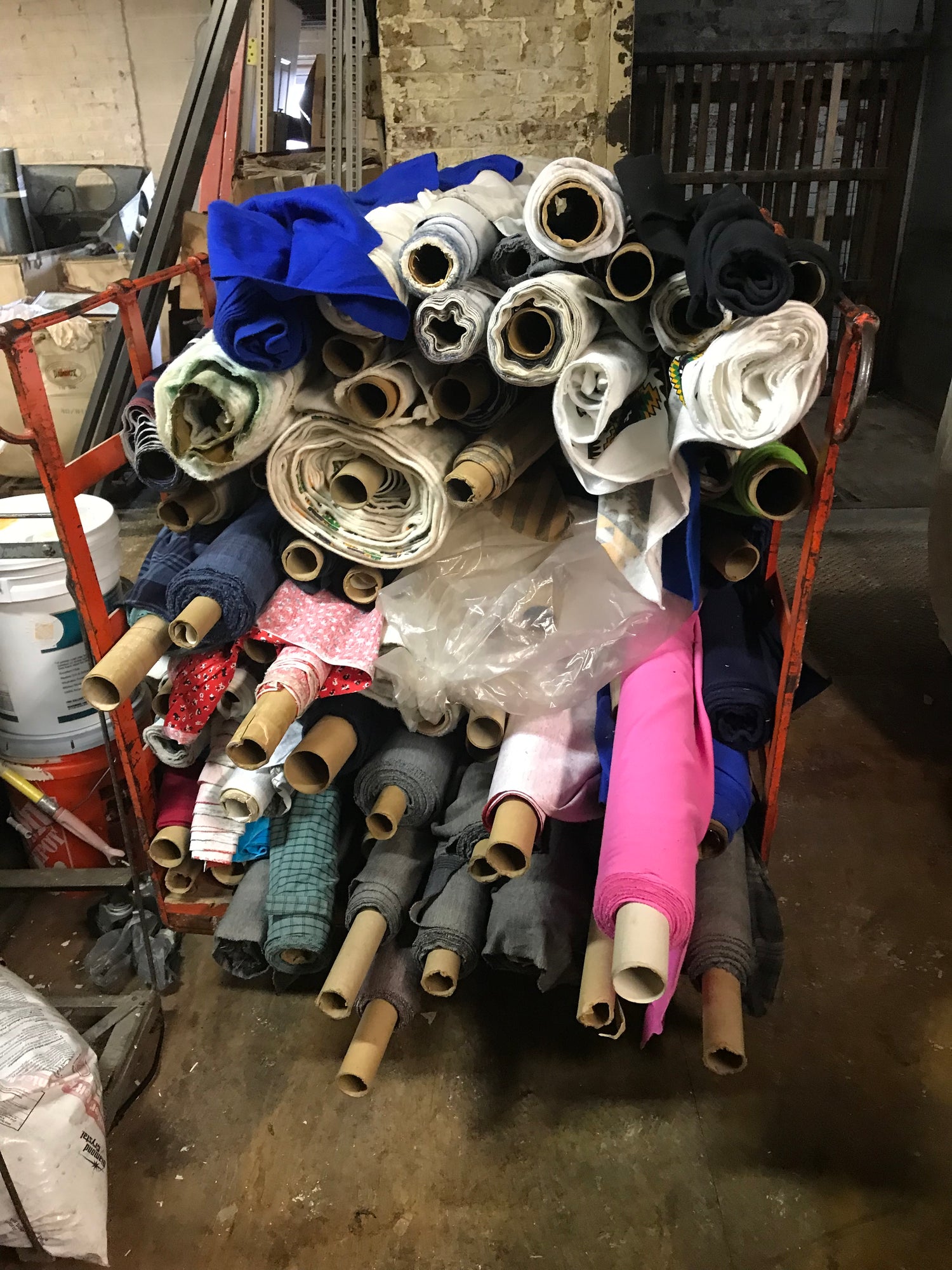 Rescued deadstock fabric rolls stacked on large cart in warehouse.